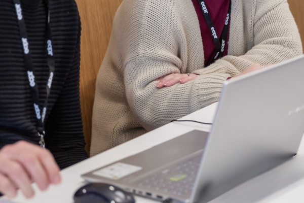 A table with two people engaged with a laptop between them.