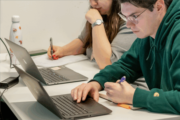 two students working on laptops in a classroom