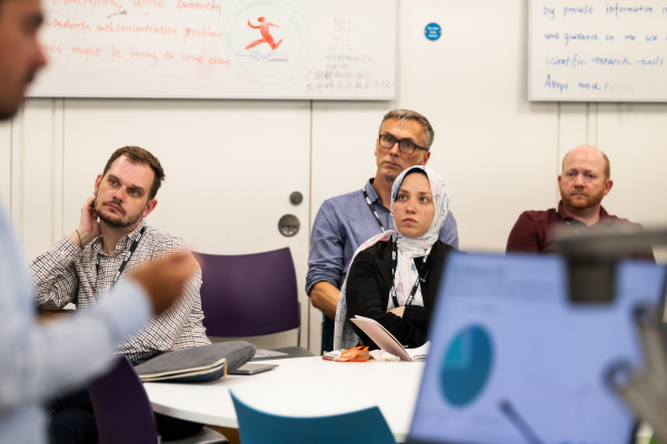 A group of people gathered around a table in a classroom setting, engaged in discussion or collaboration
