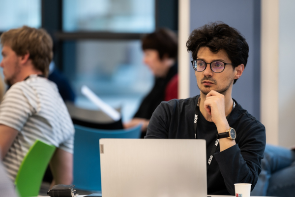 A man with glasses is sitting at a table, listening to a presentation.