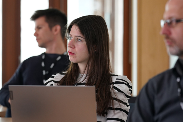 A woman in front of a laptop, with two men behind her, discussing something together.
