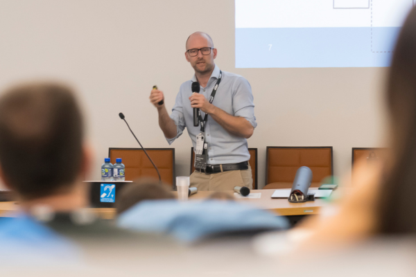 An instructor is giving a presentation to a group of people seated in front of him