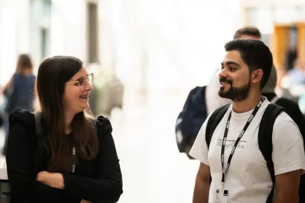 A man and woman in conversation at an ECPR event. Both are smiling and wearing lanyards around their necks.