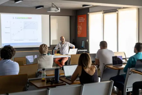 Lecturer presents a graph on 'Case Selection' to students in a bright classroom. Students have laptops open.